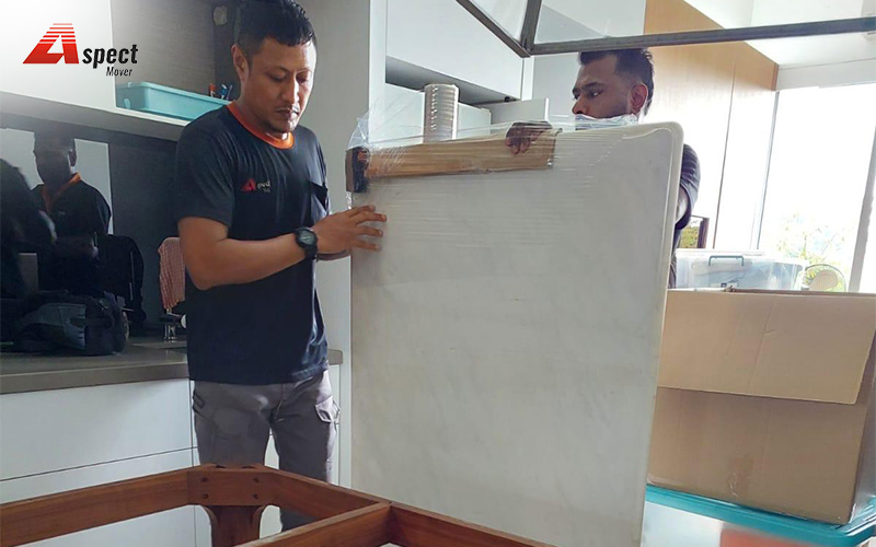 Professional movers carefully wrapping a large table in a home.
